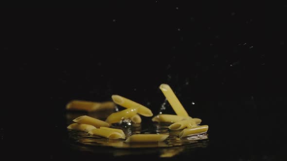 Pasta Falls In Water In Dark And Splashes Scatter In Different Directions
