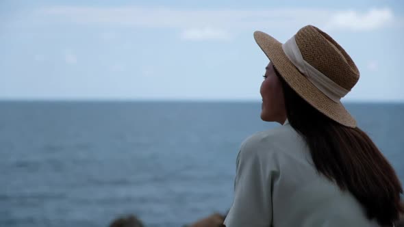 Slow motion of a young woman with hat standing and looking at the sea