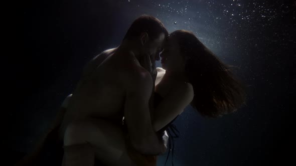 Brunette Lady and Brawny Man Are Hugging Inside Water of Pool Underwater View alt