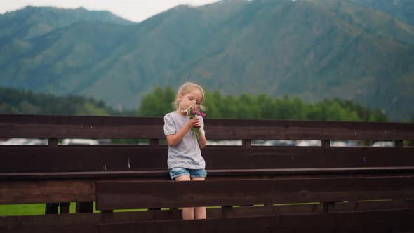 Little Girl Smells Small Bouquet of Windflowers on Bench alt