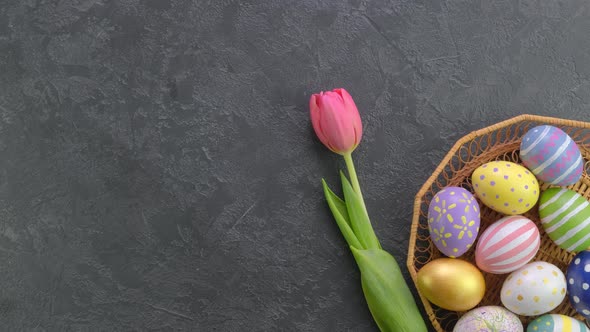 Hand Putting Down Tulips Next to Colorful Easter Eggs in Basket on Bright Background alt