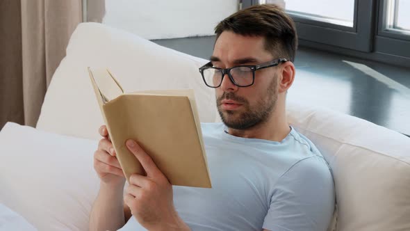 Man in Glasses Reading Book in Bed at Home