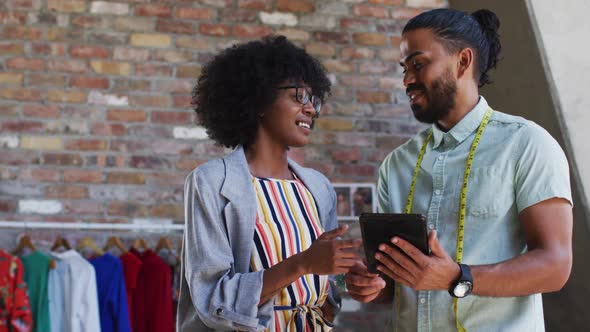 Diverse male and female fashion designers in discussion at work looking at tablet alt