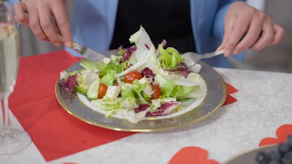 Closeup of Greek Salad in Plate with Female Hands Using Fork and Knife Mixing Ingredients alt