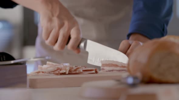 Detail of Man Hand Cutting Jowl Bacon with Knife alt