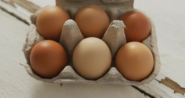 Video of overhead view of brown eggs in egg carton on rustic background alt