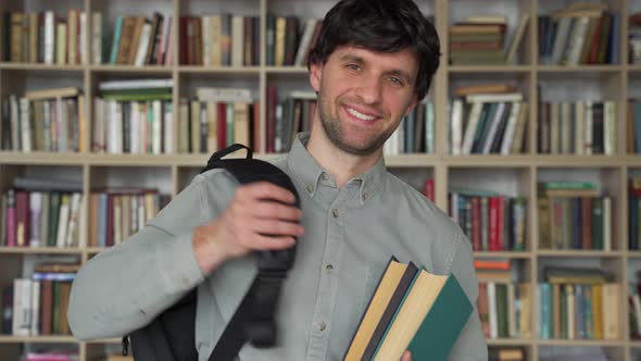 Young Man Stands with Books and a Backpack in the Library alt