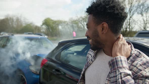 Young man rubbing neck in pain from whiplash injury standing by damaged car alt
