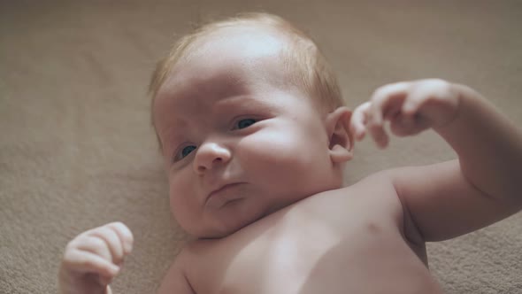 Funny Infant Boy with Cheeks and Big Blue Eyes Lies on Table alt