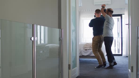 Multi ethnic gay male couple having fun dancing in bedroom alt