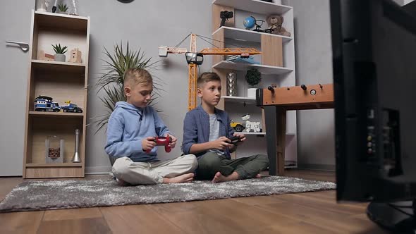 Teenage Brothers Sitting on the Carpet and Competing in Video Game Using Gamepads alt