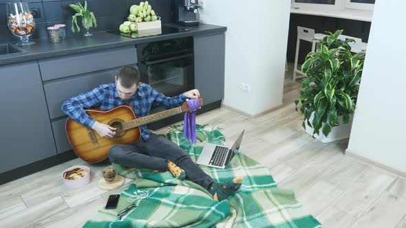 Professional guitarist tuning guitar sitting on floor in kitchen at home. alt