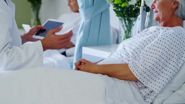 Male doctor discussing medical report with senior woman on digital tablet alt