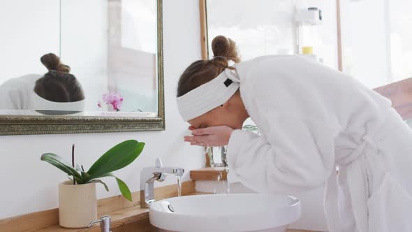 Woman in bathrobe washing her face in the sink alt