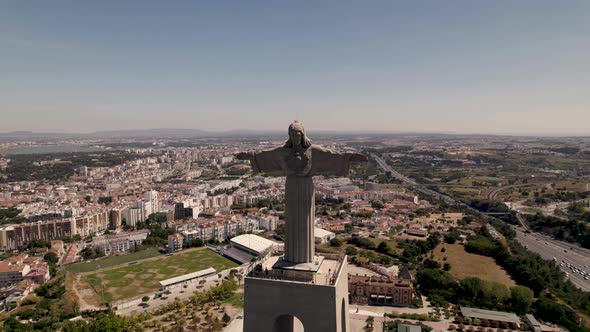 Cristo Rei, Sanctuary of Christ the King, against Almada cityscape. Aerial pullback view alt