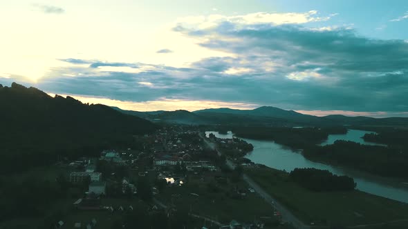 Aerial View: Small Tourist Town in the Mountains, Under Clouds. In the Twilight. Near the Mountain alt