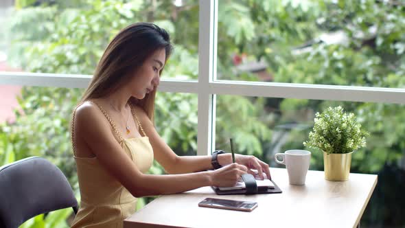 Young pretty woman writing in appointment book at coffee shop alt
