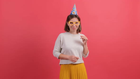 Happy Young Woman in Party Hat Holding Birthday Accessories on Red Background. alt