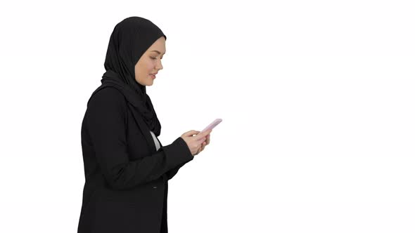Muslim Woman Messaging on Her Mobile Phone While Walking on White Background. alt