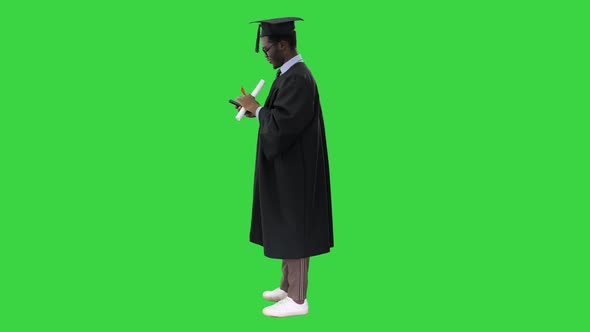 Happy African American Male Student in Graduation Robe Taking Phone Selfies with His Diploma on a alt