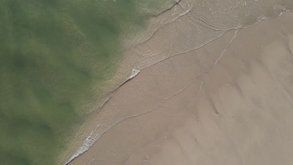 Aerial view of water rolling into coastline with seagulls flying past.