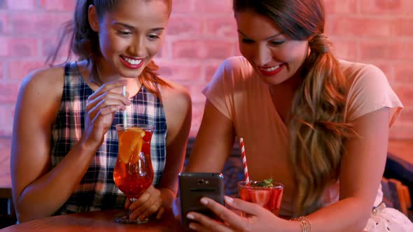 Friends using mobile phone while having cocktail alt