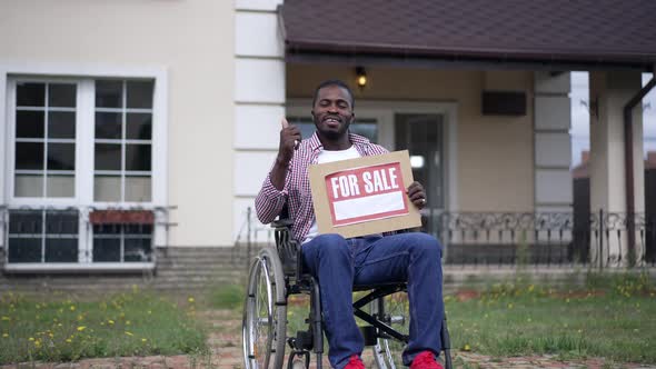 Confident Cheerful African American Disabled Sales Agent in Wheelchair Advertising House Pointing at alt