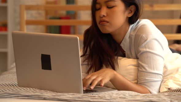 Portrait of Bored Young Asian Girl Lying Down on Bed While Working From Home in Bedroom alt