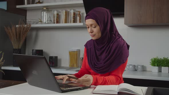 Pretty Modern Middle Eastern Woman in Hijab Using Laptop and Credit Card to Make Online Shopping alt