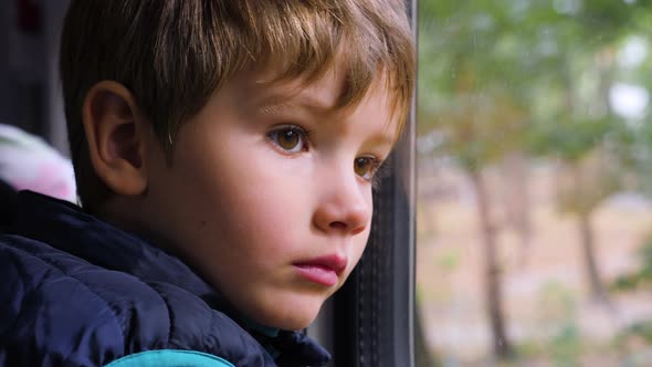 Sad Young Passenger. Close-up Shot of a Little Curious Boy Looking Out of the Window in Train alt