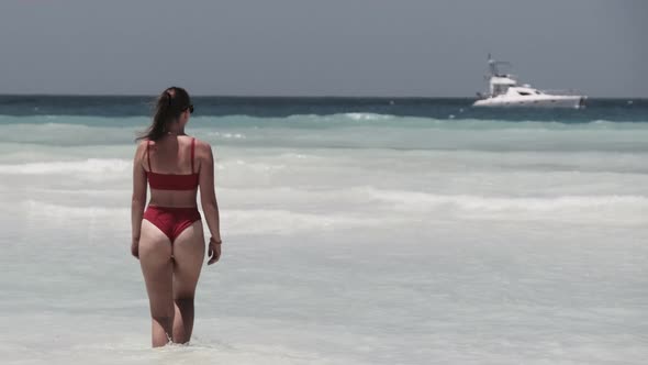 Young Woman in a Red Swimsuit Walks Into the Turquoise Ocean on a Paradise Beach alt