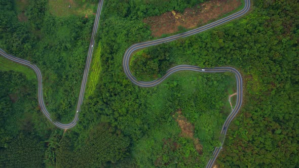 Aerial view over a winding road in the mountains of a tropical forest, Thailand. alt