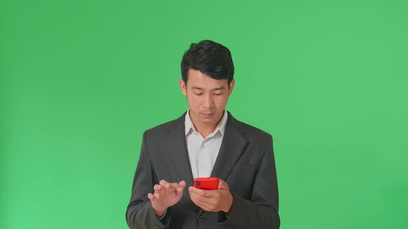 Happy Young Asian Business Man Use Mobile Phone While Standing On Green Screen In The Studio alt