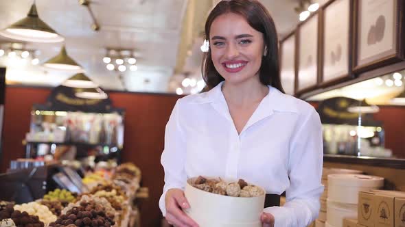 Store With Chocolate Sweets. Smiling Saleswoman Near Showcase alt