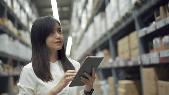 Female worker checking products with tablet in warehouse.