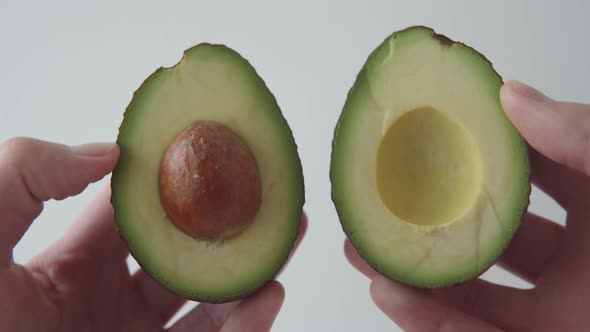 Hand Holding a Sliced Half of a Fresh Juicy Avocado with a Bone on a White Background
