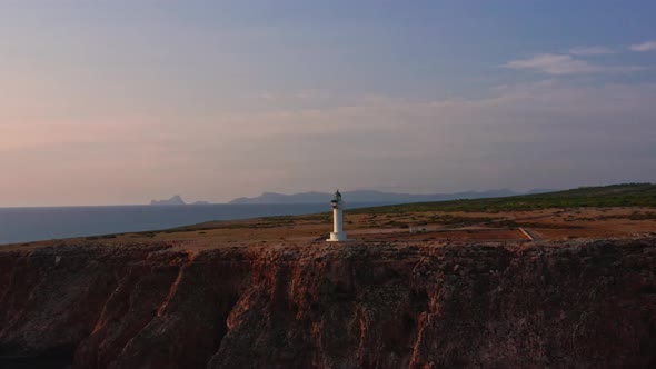 Breathtaking circle shot of lighthouse on majestic rocky cliff, golden hour alt