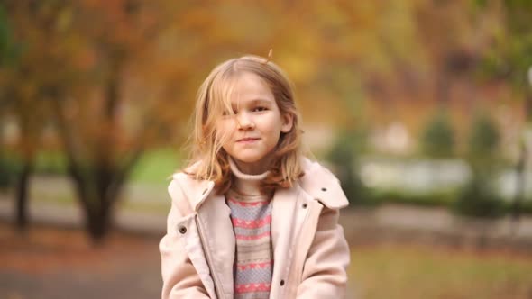 Cheerful and Sweet Little Girl Collects Fallen Autumn Leaves and Tosses alt