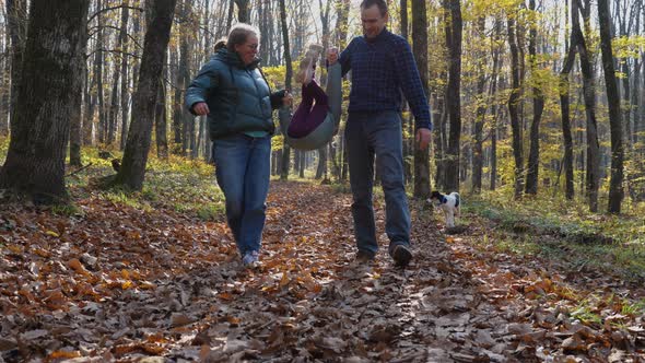 A man and a woman walk through the leaves in an autumn forest, holding hands with a child alt