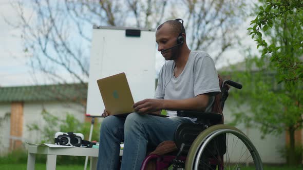 Portrait of Concentrated Serious Paralyzed Man in Wheelchair Talking at Laptop Web Camera alt