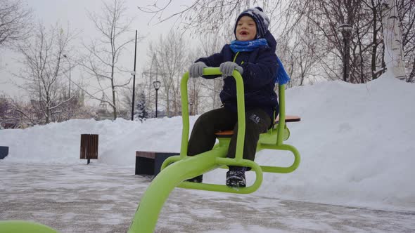 A Little Boy Swings on a Swing on the Playground in the Winter