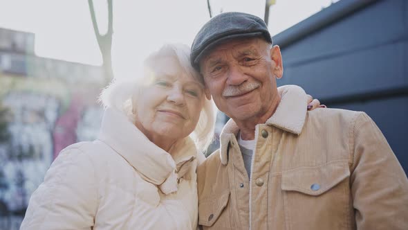 A Stylish Elderly Couple Smiling at Camera Standing on a Sunny Modern Street