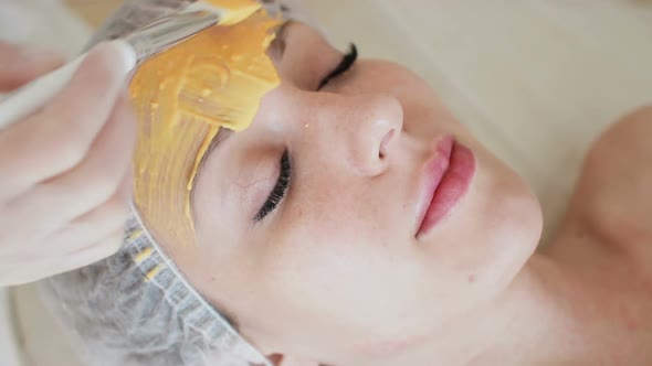 Beautician Puts a Yellow Mask on Face Woman in Spa Salon Close Up