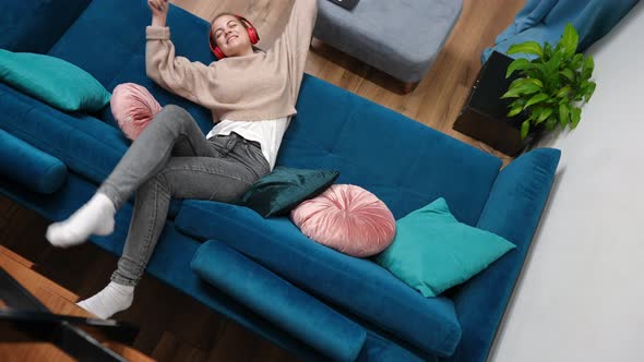 Top View Carefree Teenage Girl Lying on Couch Listening to Music in Headphones Singing alt