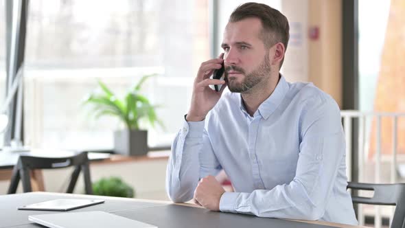 Serious Young Man Talking on Smartphone in Office alt