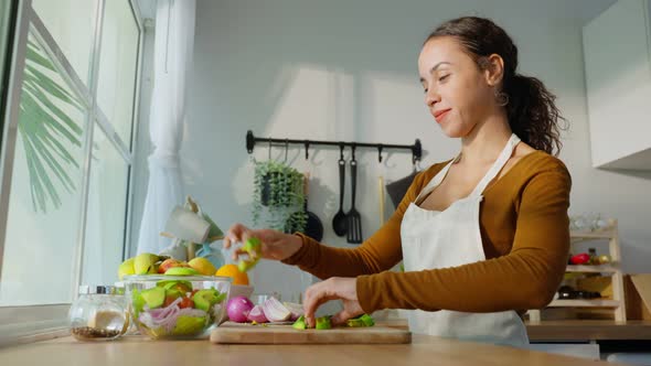 Latino attractive woman wear apron cook green salad in kitchen at home. alt