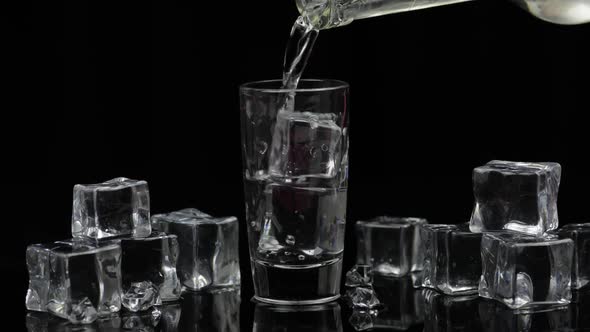 Pouring Up Shot of Vodka From a Bottle Into Glass. Black Background alt