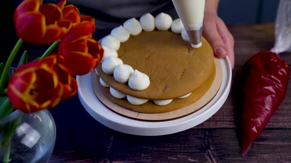 On Dark Honey Cakes From a Pastry Bag Cream is Applied in White Circles on the Sides of the Cake on