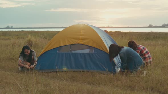 Group of a young Asian women camping pitch a tent while sunset enjoying having fun together a summer