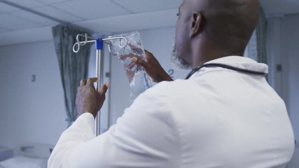 African american male doctor preparing drip bag for patient in hospital room alt